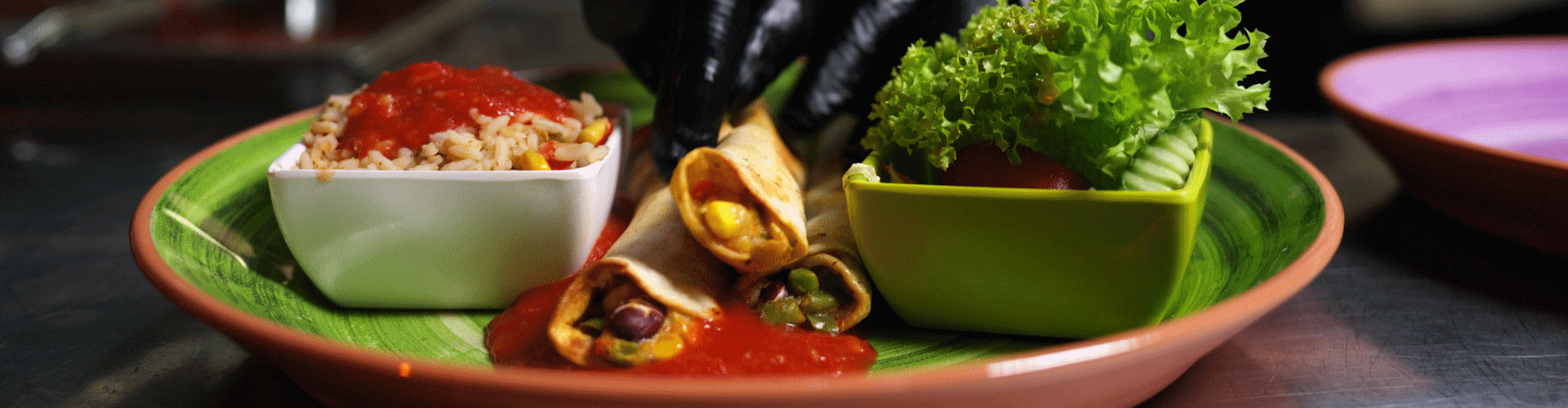 A person in black gloves plating a dish with rice, rolled tacos, sauce, and salad.