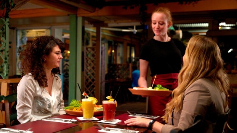 A waitress serving food to two women at a restaurant table with drinks and plates.