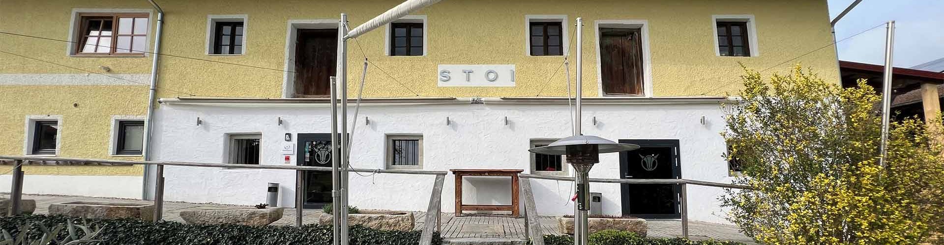 Rustikale Fassade des STOI von Ludwig Maurer mit Außenbereich und Holzmöbeln.