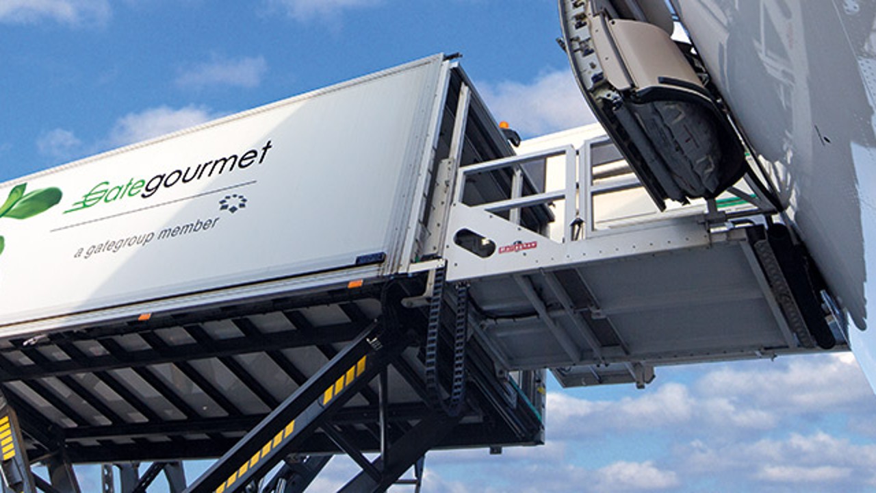 Container from Gate Gourmet being loaded onto an airplane with a blue sky in the background.