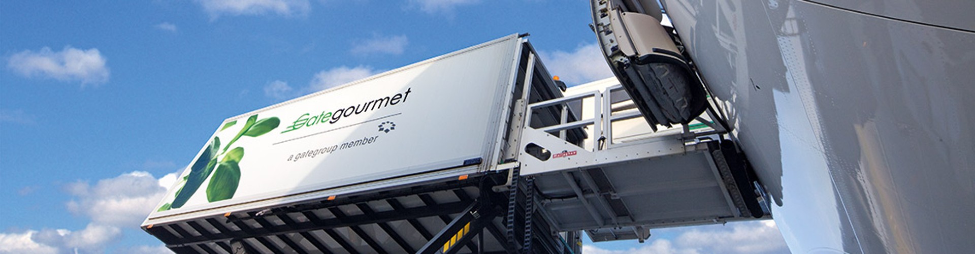 Container from Gate Gourmet being loaded onto an airplane with a blue sky in the background.