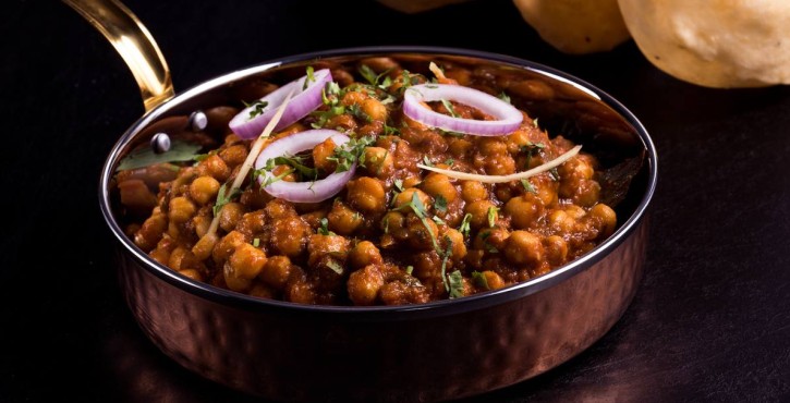Spicy Indian chickpea curry (chole) garnished with onions and herbs, served with puri.