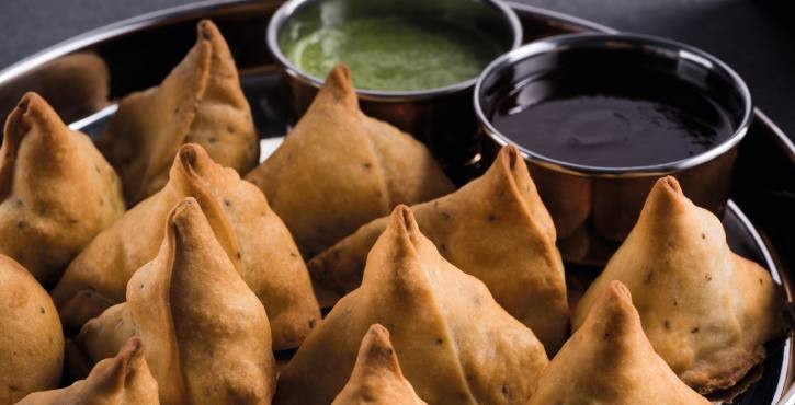 Plate of crispy samosas served with green and tamarind chutneys.