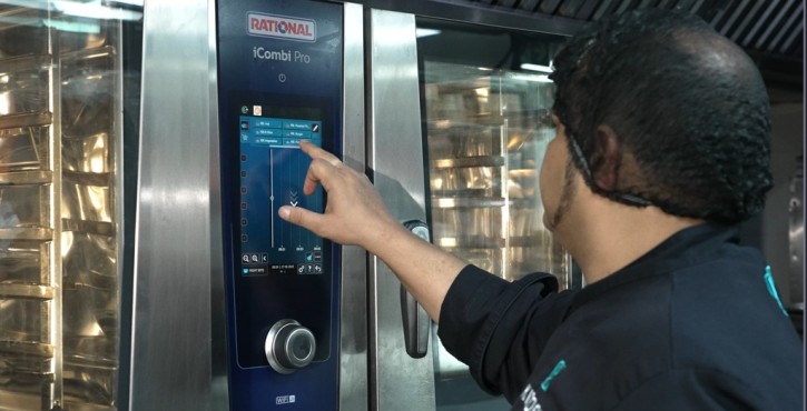 Chef adjusting the RATIONAL iCombi Pro combi oven touchscreen in a professional kitchen.