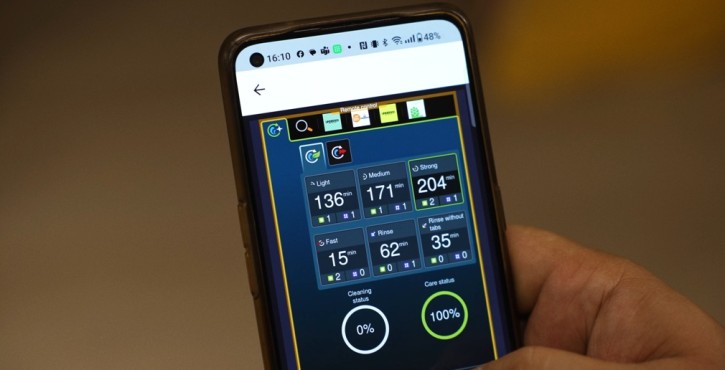 Hand holding a smartphone showing remote cleaning controls for a combi oven.