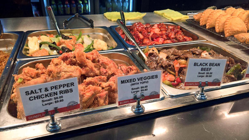 Buffet station showcasing a variety of dishes including salt & pepper chicken ribs, mixed veggies with tofu, and black bean beef, with labels displaying names and prices.
