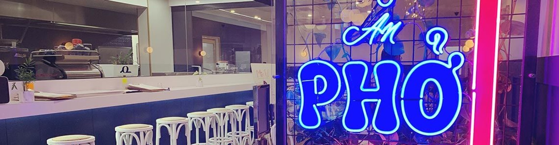 Neon sign reading "An Pho" in a restaurant with a modern bar and high stools.