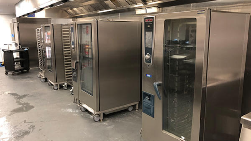 Industrial kitchen featuring multiple large RATIONAL appliances, including ovens and refrigerators, arranged in a clean, spacious area.
