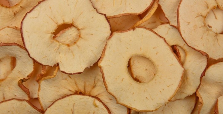 Close-up image of dried apple slices with peels and core holes, spread out in a layered pattern.