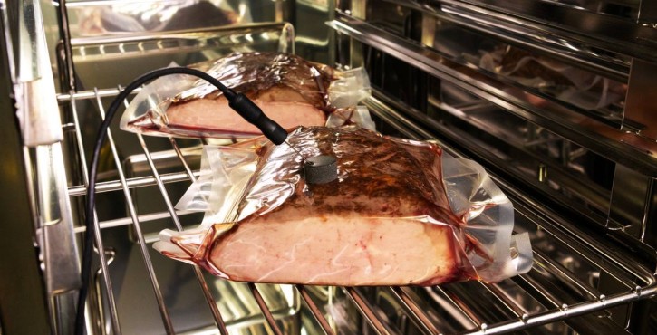 Vacuum-packed meat portions cooking sous-vide in a combi oven, with a core temperature probe inserted.