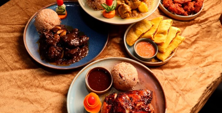 Assorted Jamaican dishes with rice, glazed chicken, curry, patties, and fried wings on a table.