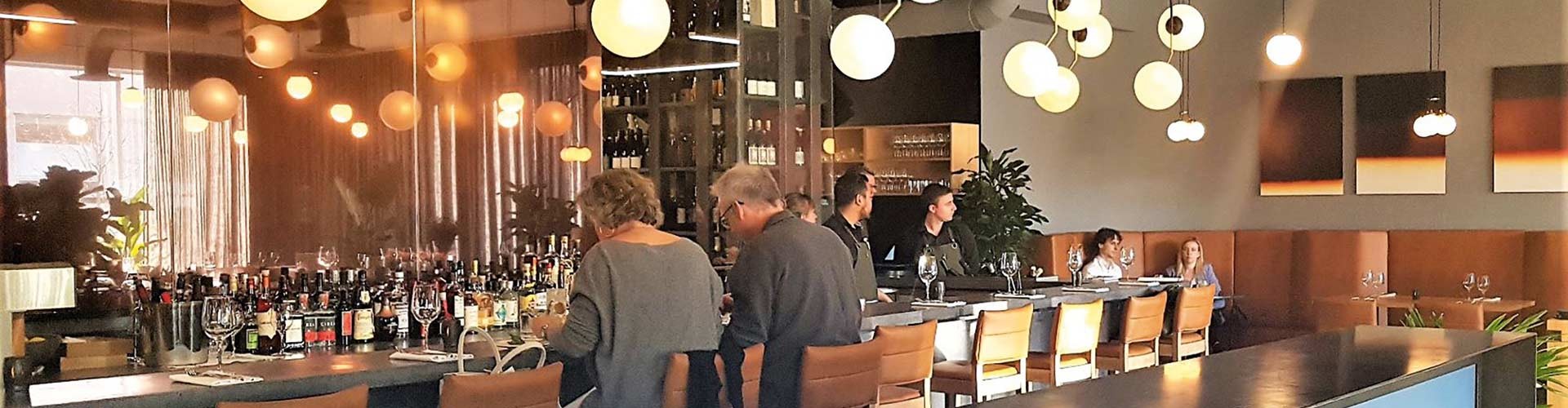 Warm restaurant interior with bar seating, pendant lights, and guests dining.