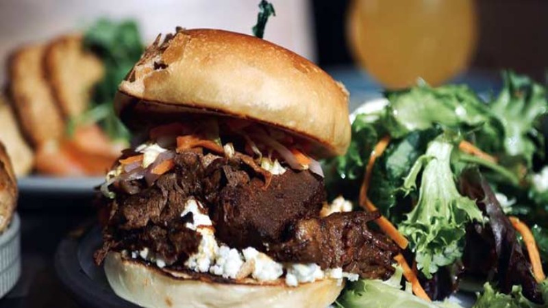 Close-up of a pulled pork burger with toppings and a side salad, served on a plate.