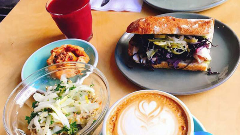 A table setting featuring two sandwiches, a bowl of salad, a latte with a heart design, and a cup of coffee.