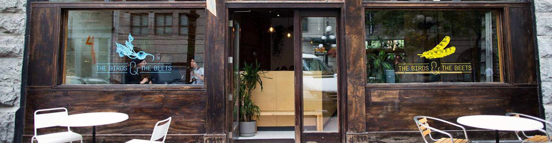 The front view of a café with a wooden door and large windows, showcasing colorful signage.