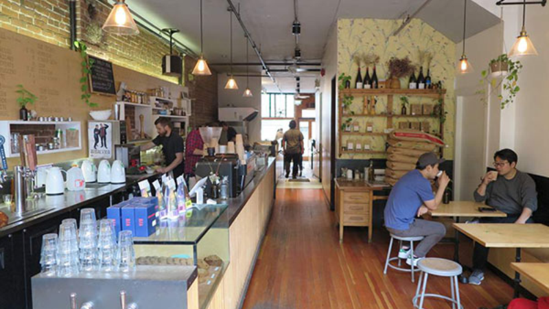 The interior of a café featuring a wooden counter, seating areas, and staff preparing drinks.