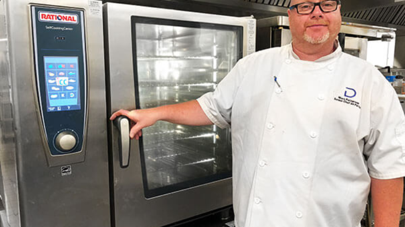 Chef standing beside a Rational oven in a kitchen.