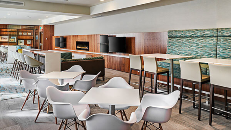 Modern restaurant seating area with tables, chairs, and TVs on the wall.