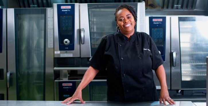 Chef smiling in front of RATIONAL iCombi Pro combi ovens in a commercial kitchen.