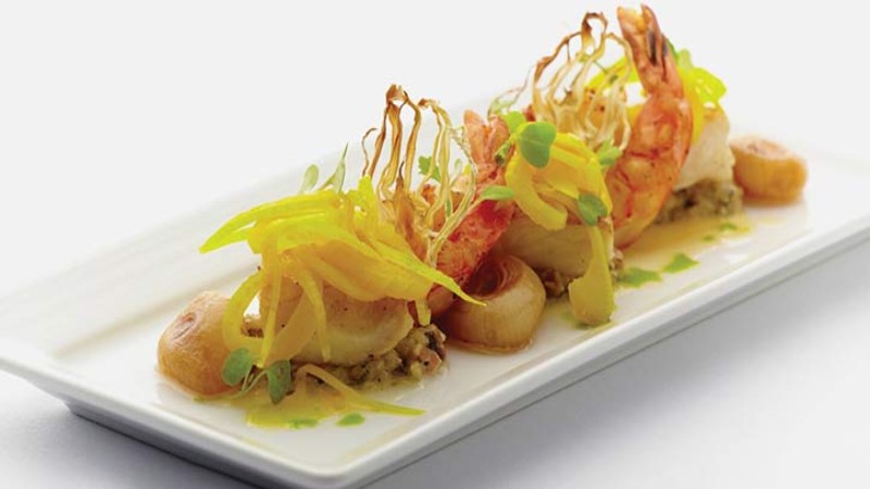 A gourmet dish with shrimp, vegetables, and a drizzle of sauce on a white plate.