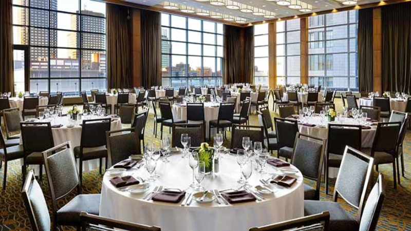Elegant dining room with round tables set for dinner, large windows, and city view.