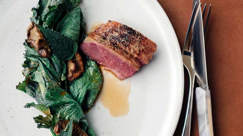 A plate with a slice of meat, sautéed greens, and mushrooms.