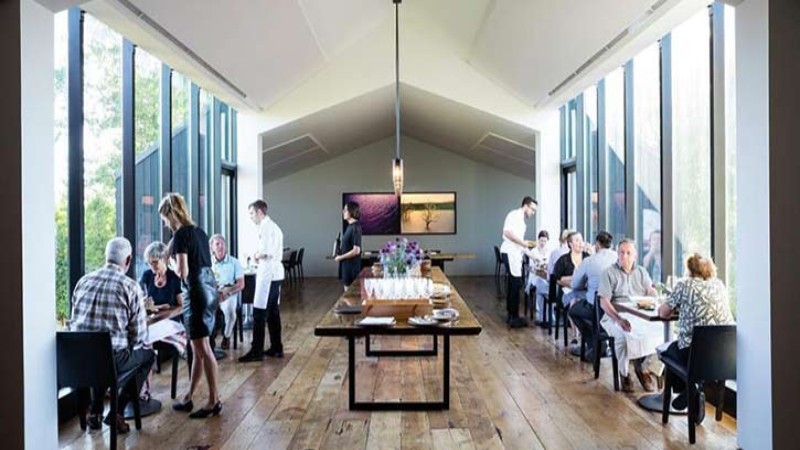 A restaurant dining room with guests seated, servers attending, and large windows letting in natural light.
