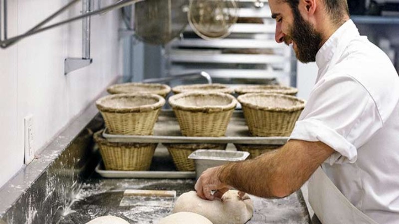 A baker working with dough in a kitchen with baskets in the background.