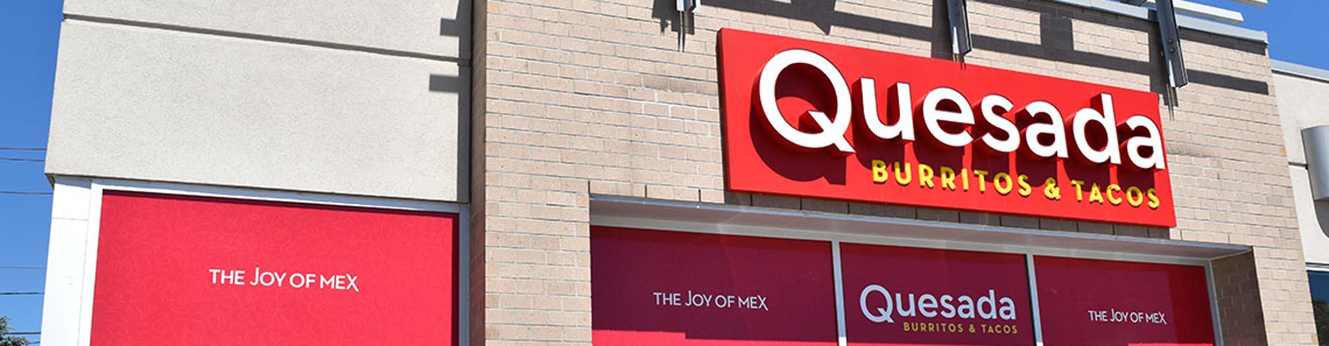 The exterior of a Quesada Burritos & Tacos restaurant with red signage displaying the name and slogan ‘The Joy of Mex‘.