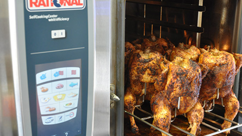 Rational SelfCookingCenter oven with several whole chickens roasting on skewers inside the unit.