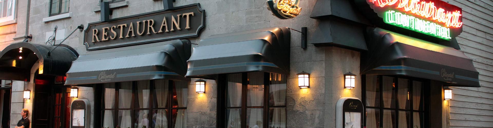 A restaurant with a traditional facade, outdoor plants, and a neon "RESTAURANT" sign.