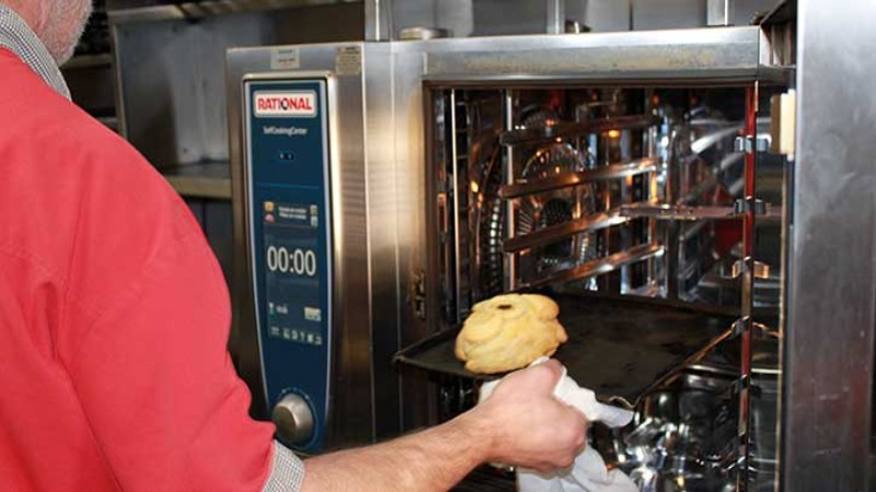 A chef removing a freshly baked item from a Rational oven in a kitchen.