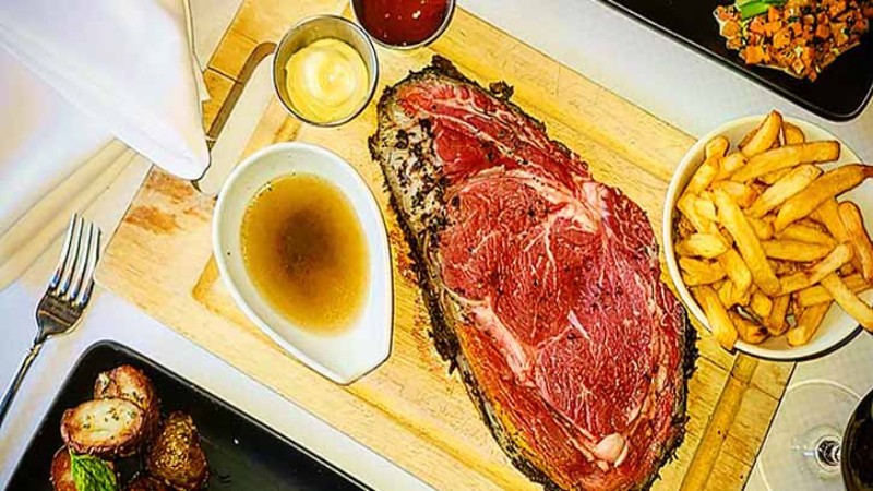 A large steak served with fries, sauce, and side dishes of roasted potatoes and vegetables.