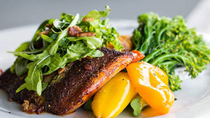 A plate of grilled fish with yellow peppers, broccoli, and a fresh green salad.