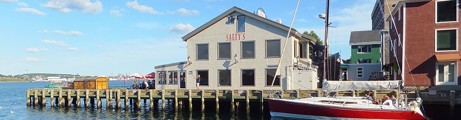 A waterfront view of a building with a dock and a sailboat tied to the pier.