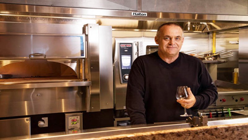 A person standing in a professional kitchen at Hilton, holding a wine glass, with cooking equipment in the background.