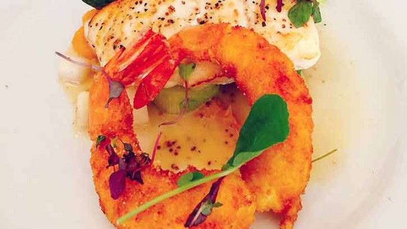 A plate with fried onion rings, fish, and garnished with herbs and a creamy sauce.