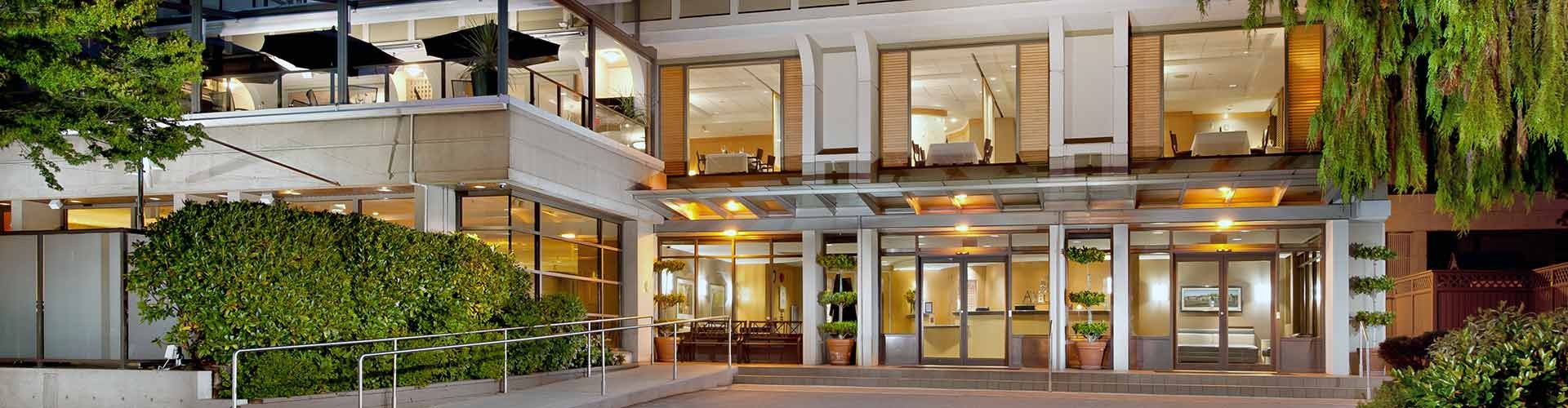 The front view of a modern building with a balcony, lush greenery, and a sunset sky.