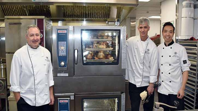 Three chefs standing together next to a Rational oven with roasting chicken inside.
