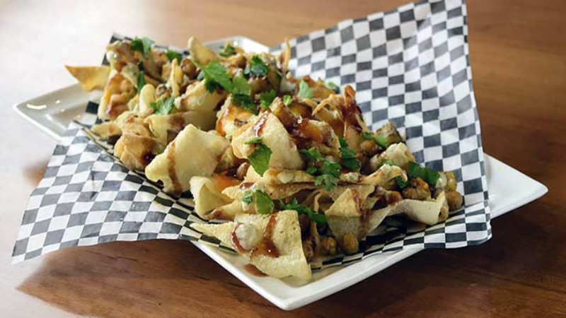 A plate of nachos topped with cheese, chickpeas, onions, and cilantro, served on a black and white checkered paper liner.