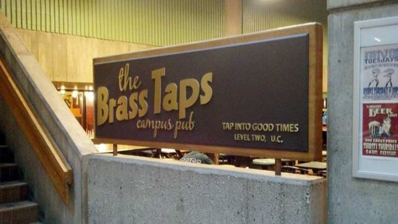 Sign for "The Brass Taps Campus Pub" at a university, indicating its location on level two, encouraging visitors to "Tap into good times.