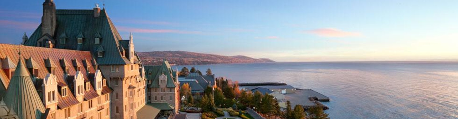 Vue du Château Frontenac, avec des jardins verdoyants et l‘océan en arrière-plan au coucher du soleil.