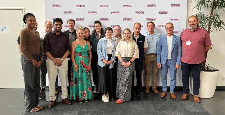 Group of consultants posing together in front of a RATIONAL welcome wall.
