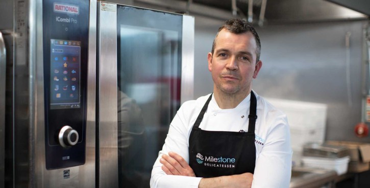 Chef Cathal Grant stands beside a RATIONAL iCombi Pro combi oven in the Milestone Delicatessen kitchen.