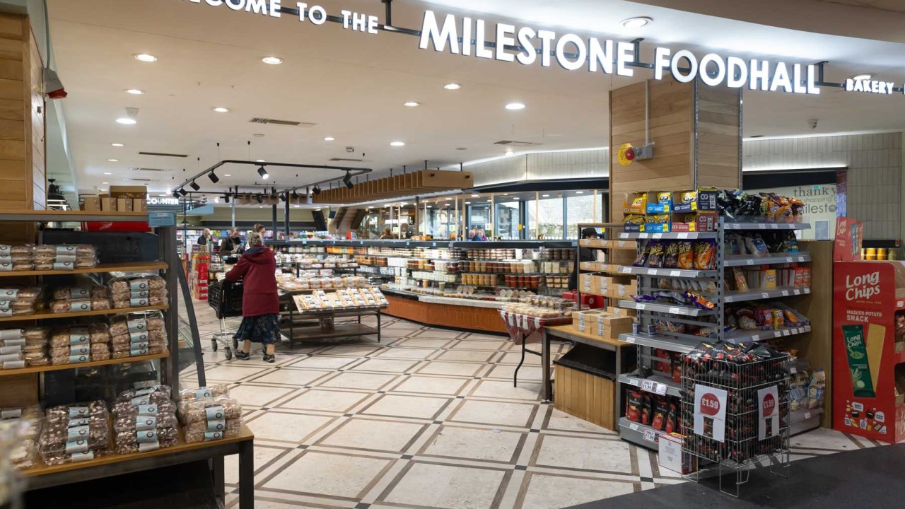 Shoppers browse bakery and snack aisles beneath the Milestone Foodhall sign in a bright supermarket hall.