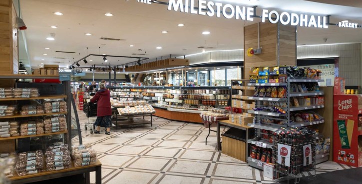 Shoppers browse bakery and snack aisles beneath the Milestone Foodhall sign in a bright supermarket hall.