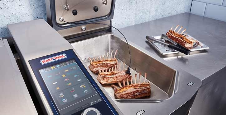 A view of a Rational iVario Pro appliance with lamb racks cooking inside, featuring a core temperature probe and a modern control panel.