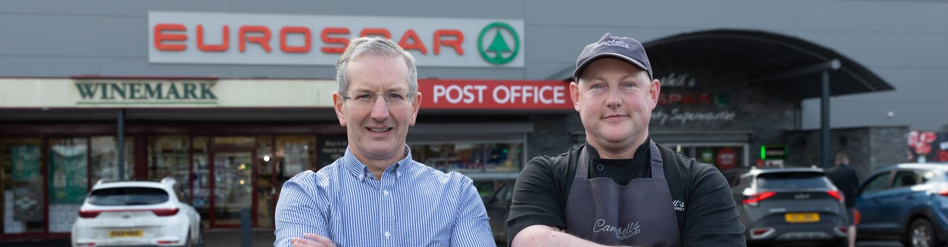 Two men standing outside Campbell‘s Eurospar supermarket with folded arms.