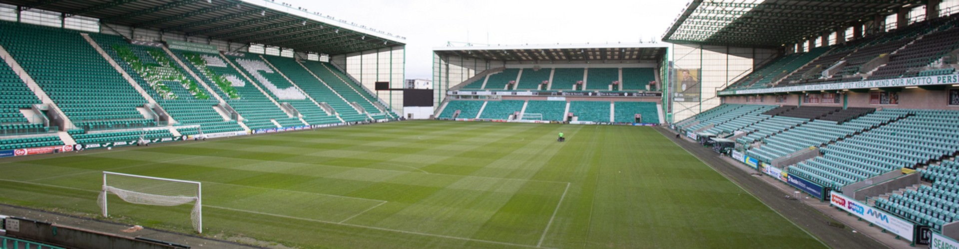Wide view of Hibernian football stadium with green pitch and empty stands.