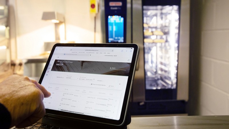 Tablet displaying HACCP data in front of a RATIONAL combi oven in a professional kitchen.